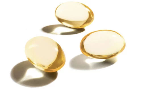 Beyaz zeminde gölgeleri vuran 3 adet altın rengi omega-3 kapsülü
