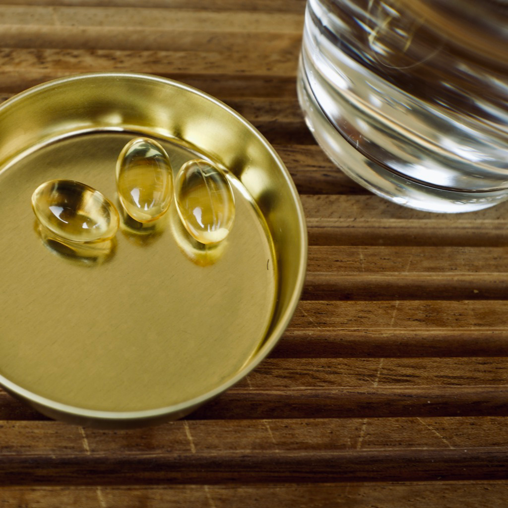 Ahşap zeminde kapağın içinde 3 adet küçük omega-3 kapsülü ve bir bardak su