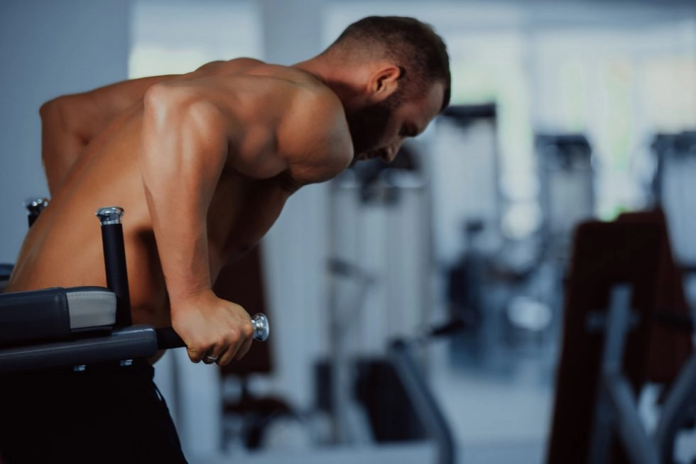 Fitness salonunda paralel bar egzersizi yapan, üst vücut kaslarını çalıştıran atletik bir erkek.