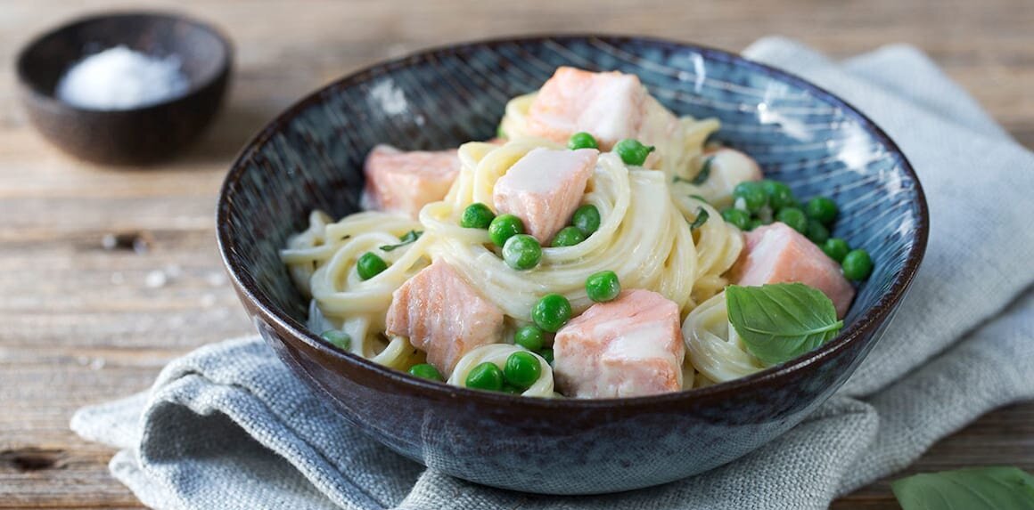 Bezelye, somon parçaları ve kremalı spagetti ile hazırlanmış lezzetli bir somonlu makarna tabağı, koyu seramik kasede servis edilmiş.