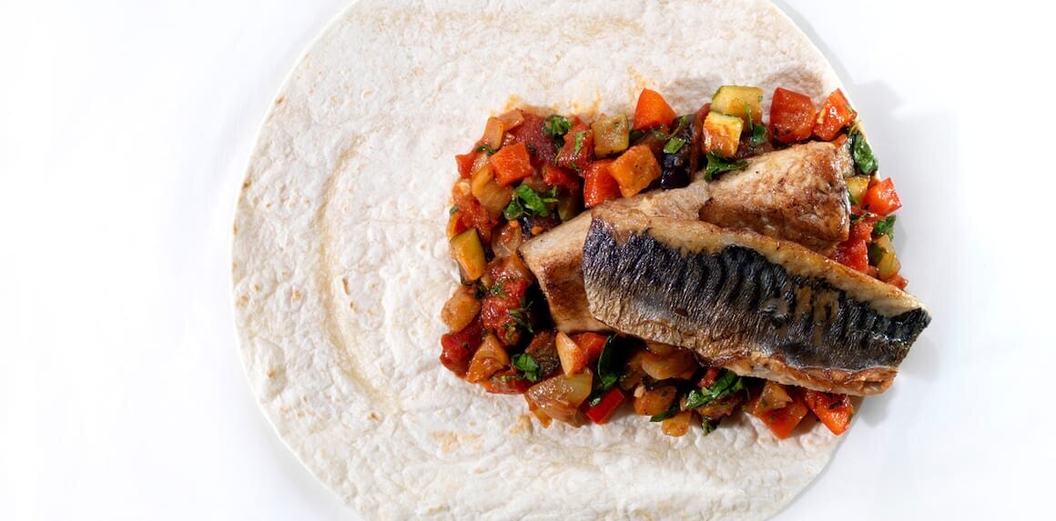 Tortilla ekmeğinin üstünde sotelenmiş sebzeler ve iki parça uskumru fileto