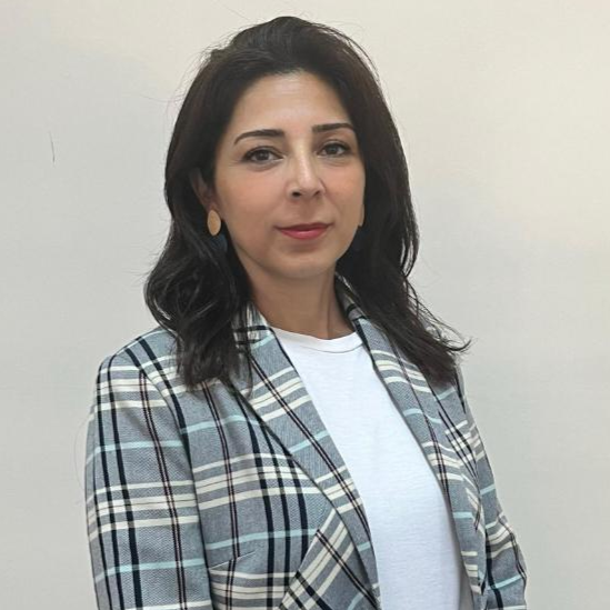 Açık renk duvar önünde duran, beyaz tişört ve kareli ceket giymiş, koyu saçlı ve ciddi ifadeli Derya Karakoyun portresi.