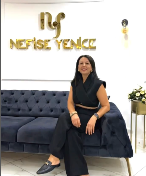 Siyah takımıyla koyu mavi kadife koltuğa oturmuş bir kadın, arka planda altın renkli 'Nefise Yüce' logosuyla beyaz ve şık bir iç mekânda gülümseyerek poz veriyor.