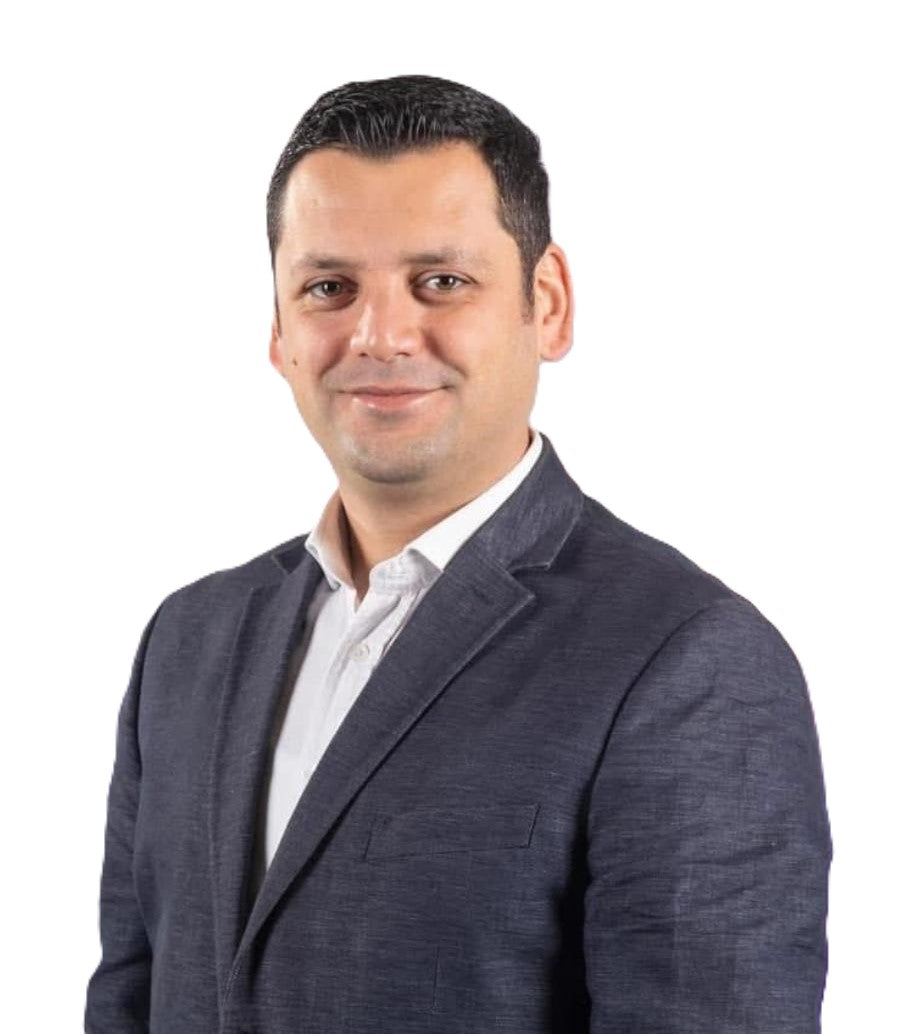 Lacivert ceket ve beyaz gömlek giymiş, kısa koyu saçlı ve hafif tebessüm eden bir adam beyaz arka plan önünde poz veriyor.